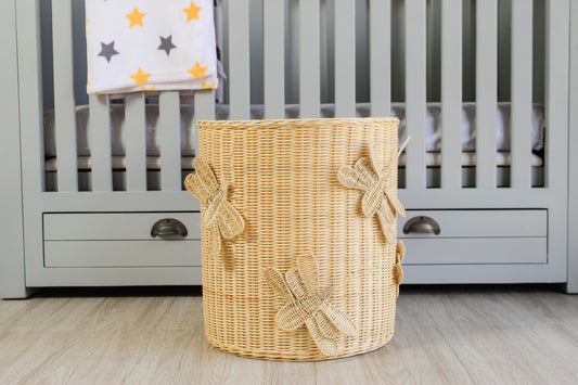 Wicker laundry basket sits in front of a gray baby crib. Insect, butterfly and dragonfly theme hamper, toy storage basket.