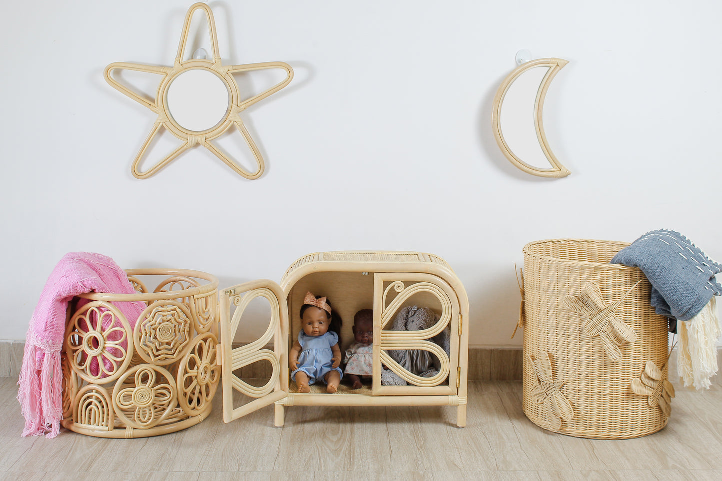 Rattan wall decor in the shape of a moon and star sits above a butterfly inspired dolls clothes wardrobe with a circle basket and a wing inspired basket