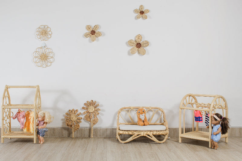 A girls bedroom or kids playroom with a scene of rattan doll play furniture. Includes hand-made rattan flower wall decor, a dolls wardrobe, dolls clothes hanger, doll sofa, doll couch, doll dresser, doll clothes and dolls