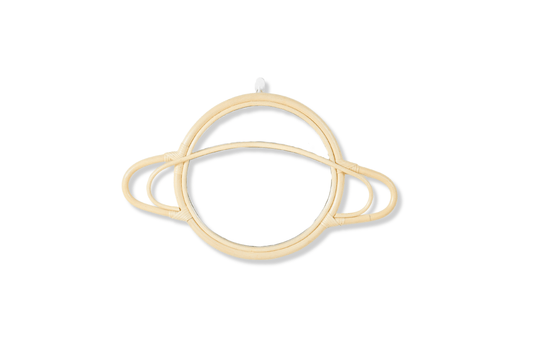 A cosmic themed wall mirror in the shape of Saturn. Sits on a white wall and the mirror is made of rattan. 