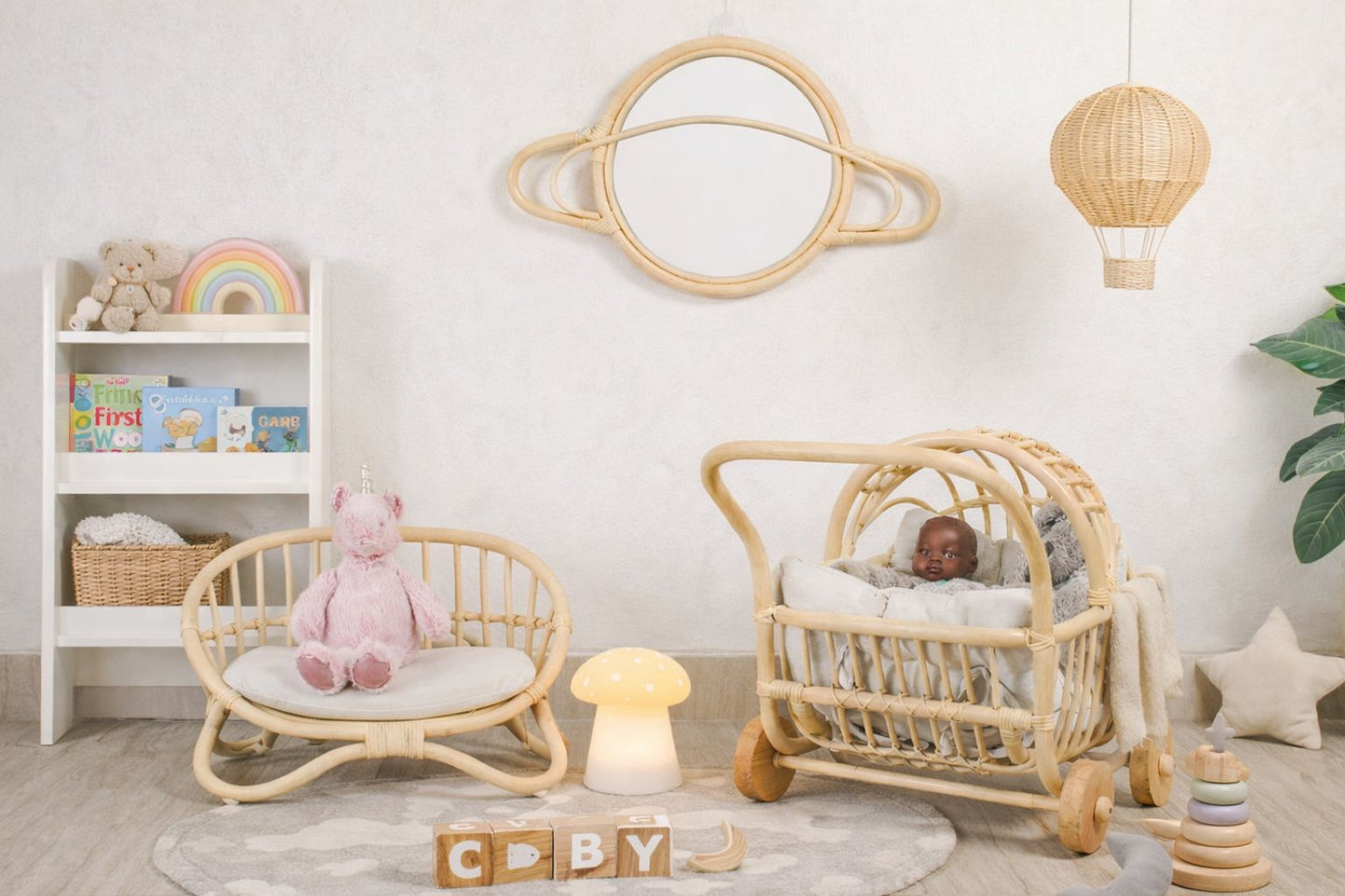A close-up view of the white linen cushion on the miniature rattan love seat. Resting on the cushion are tiny, curated details: a fabric-bound miniature book titled "Dolly's Tales" and a delicate, blue-and-white floral patterned teacup and saucer, creating a perfect vignette for toys and games.