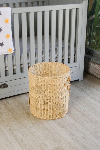 Wicker laundry basket with dragonfly design on a wooden floor next to a crib. Rattan made toy storage for kids toys. Basket for toys