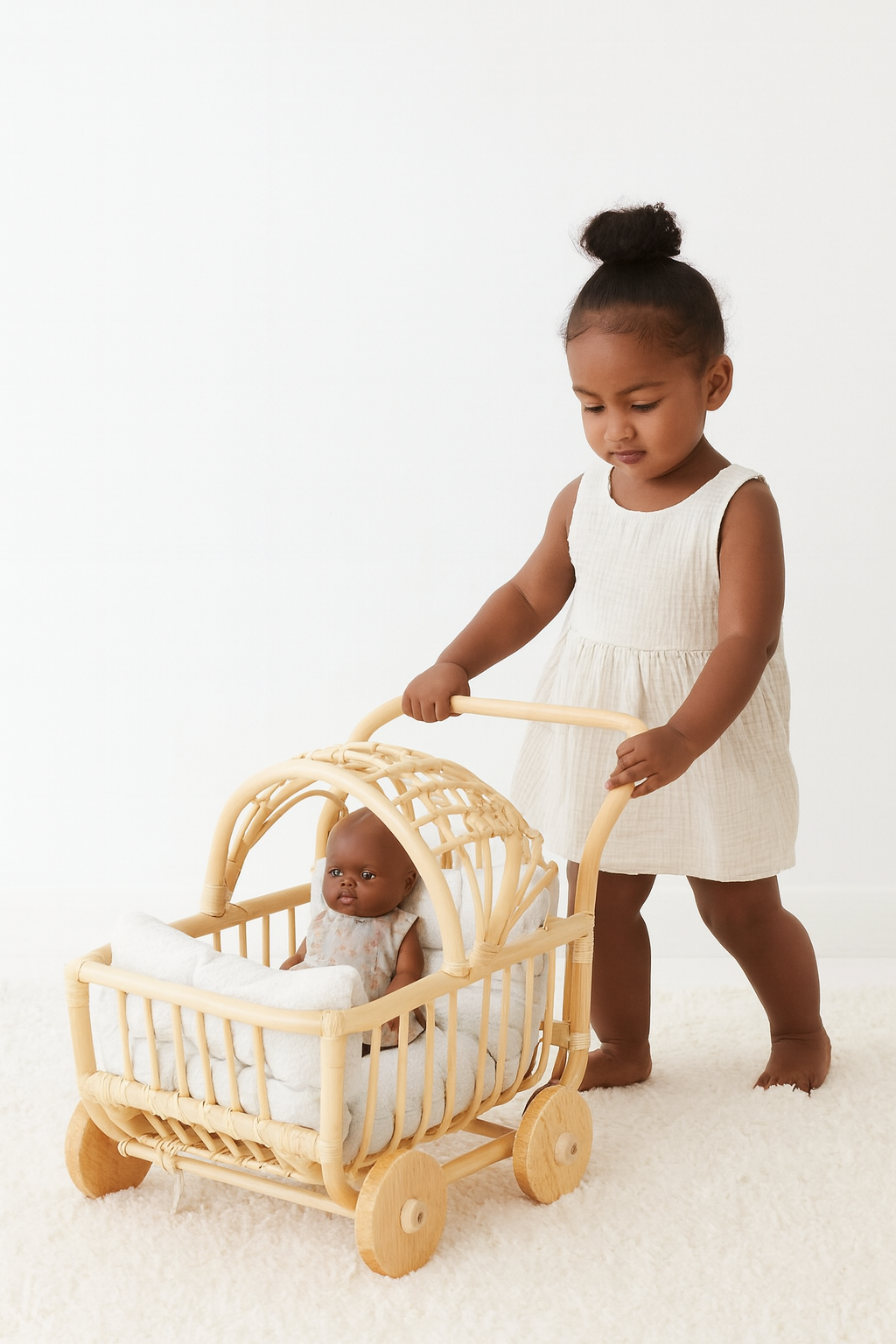 A black girl in a white dress pushes a black doll in a toy stroller or toy buggy