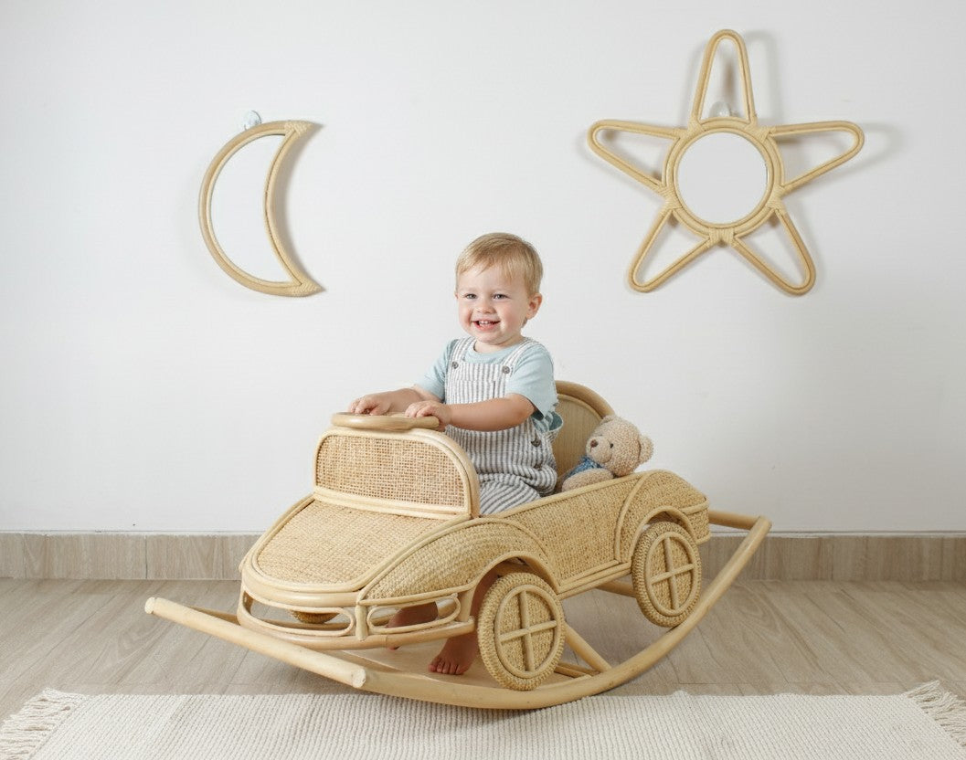 Child sitting in a wicker car rocker with decorative moon and star wall art in the background.