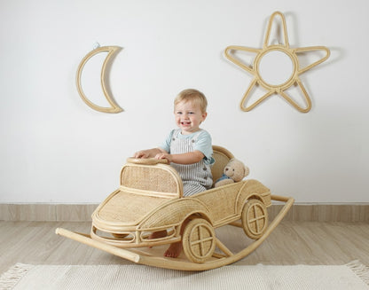 Child sitting in a wicker car rocker with decorative moon and star wall art in the background.