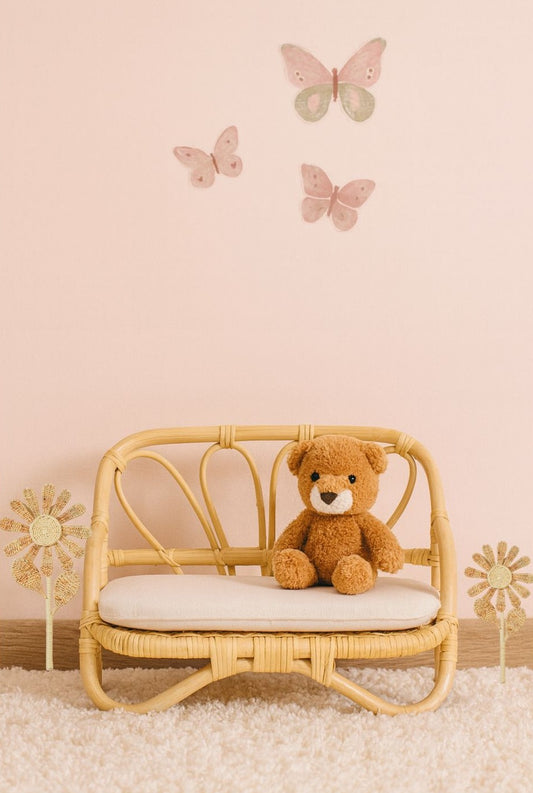 A teddy bear sits on a cute dolls lounge with flowers each side for decoration. There are pink butterflies on the pink wall behind. A fun dolls accessory toy. 