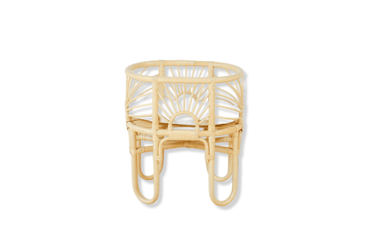 A rattan made dolls bed with sunrise shaped arches sits with a cushion and a white background. 