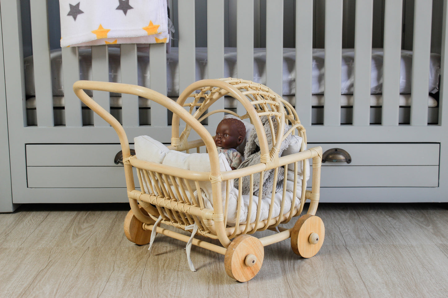 Toy baby carriage with a doll inside on a wooden floor in a nursery.