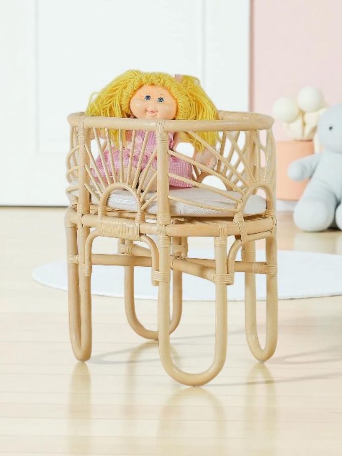 Dolls bassinet made of natural rattan material with a cushion and a cabbage patch doll sitting in it. 