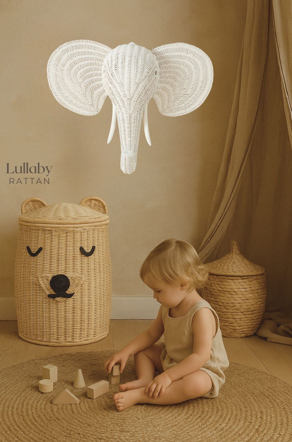 boy plays on grass mat with wooden blocks with a teddy bear hamper and white rattan elephant head wall decoration