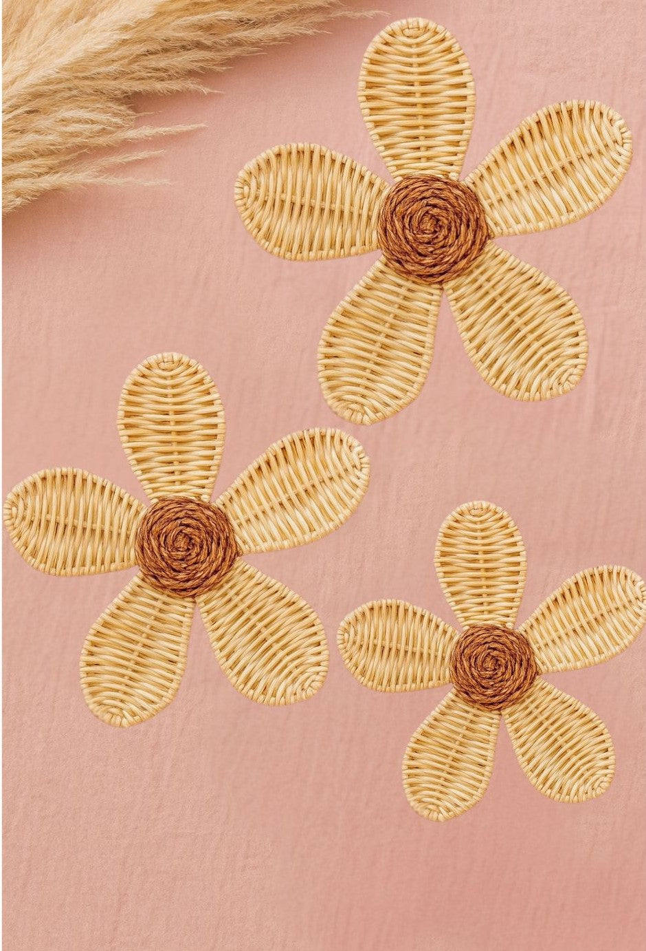 Three hand-made rattan flowers sitting on a pink rug with dried flowers beside it. It is a cute and girly scene. 