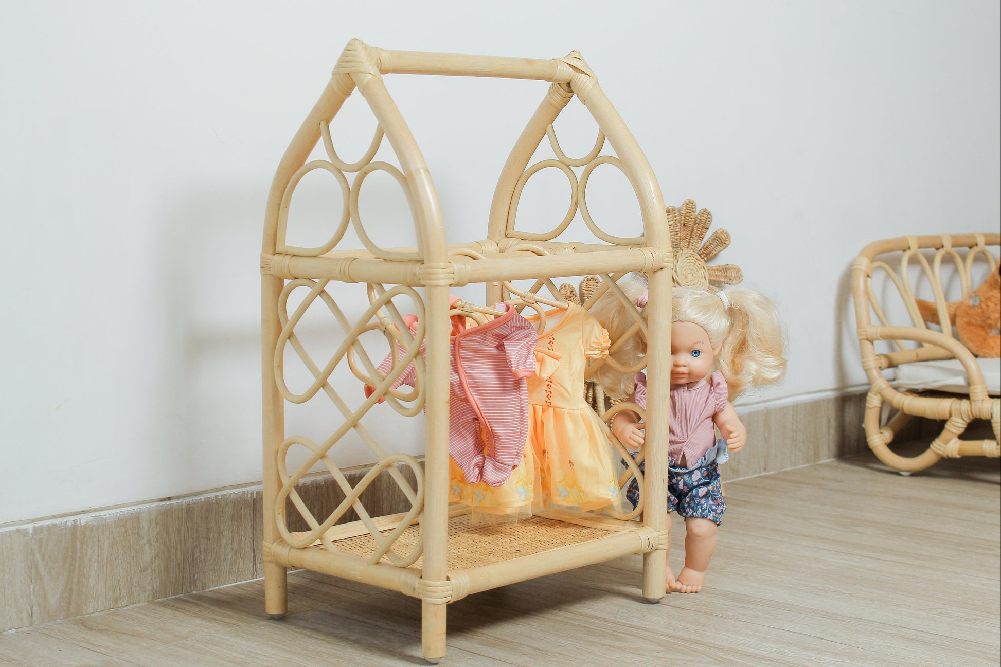 Wicker dollhouse with dolls inside on a wooden floor.