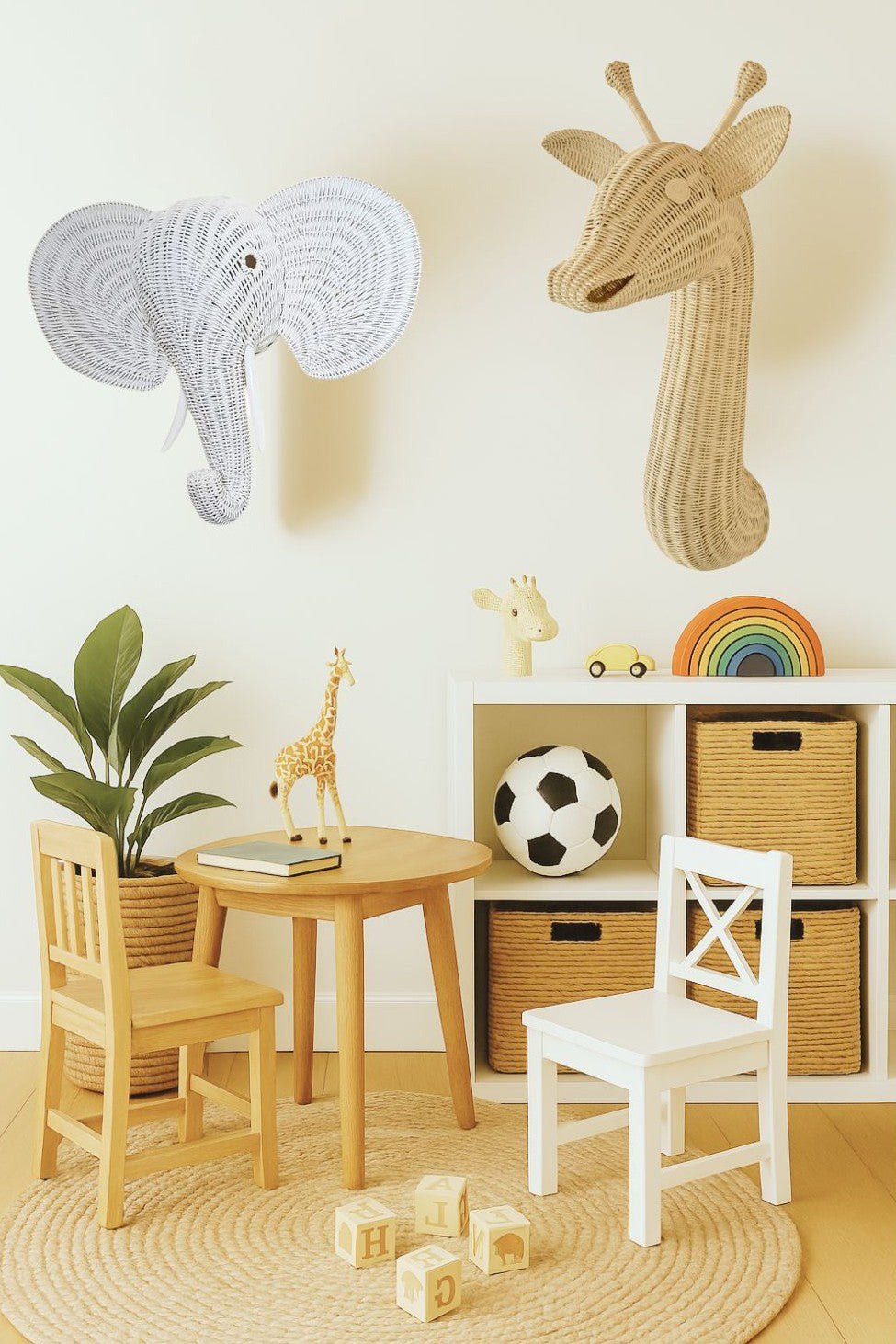 Children's room with wall decorations, furniture, and toys. A rattan elephant head and rattan giraffe head sit on the wall behind kids toys and kids table. 