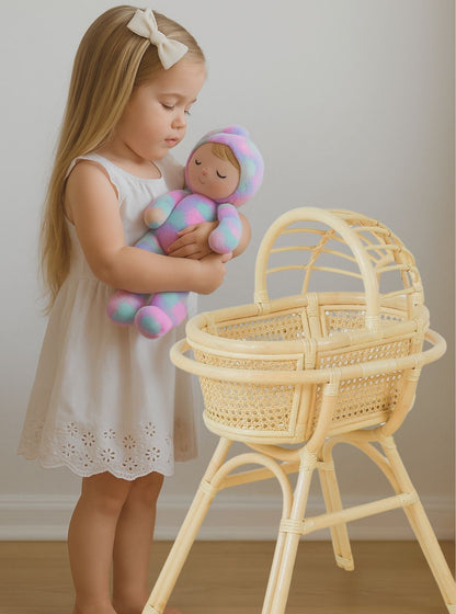 Young girl holding a colorful baby doll next to a wicker bassinet. Doll bed