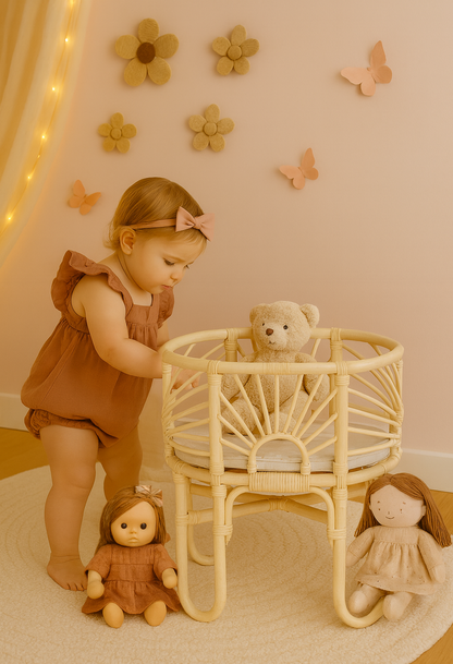 Child playing with a teddy bear in a small crib surrounded by dolls in a softly lit room. Dolls sit on the floor with butterflies on the wall and flowers. 