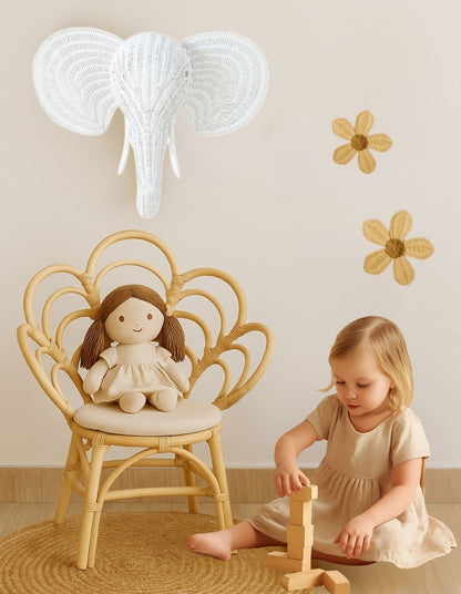 Child playing with a wooden toy on the floor, next to a chair with a doll and an elephant decoration on the wall.