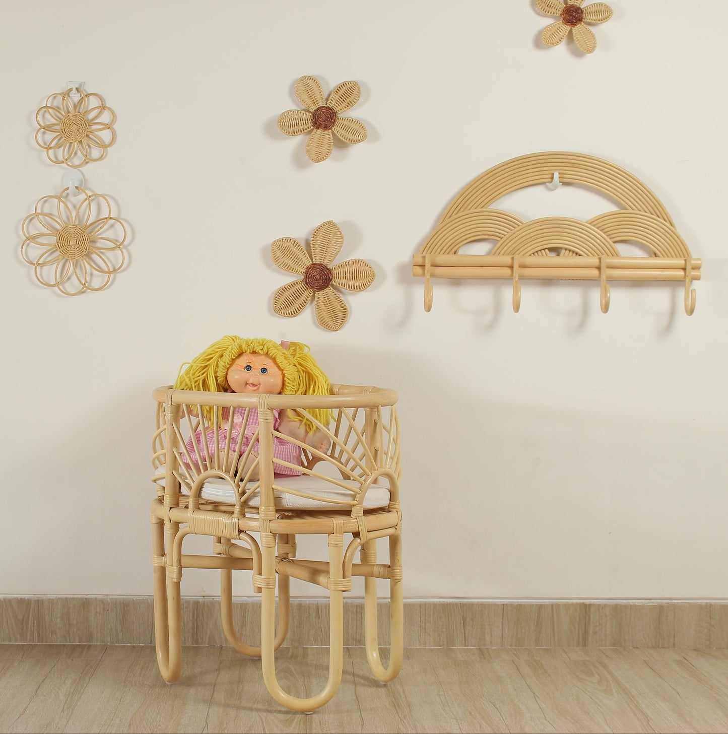 Wooden crib with a doll inside, surrounded by decorative flowers on a light-colored wall.