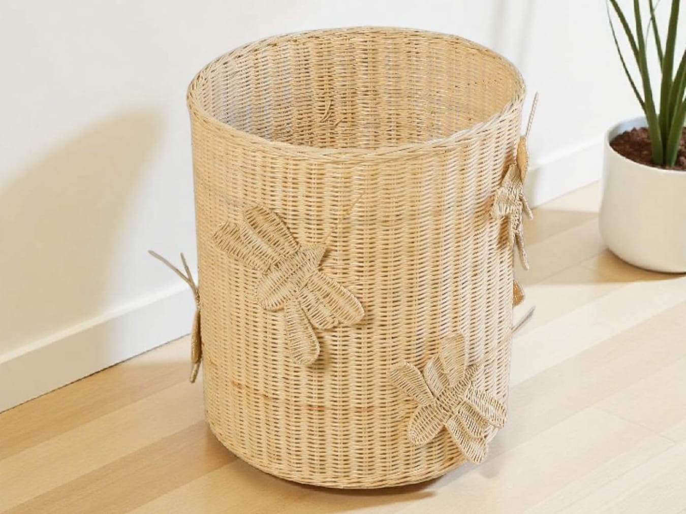 Wicker laundry basket with dragonfly designs on a wooden floor. Butterfly inspired toy basket