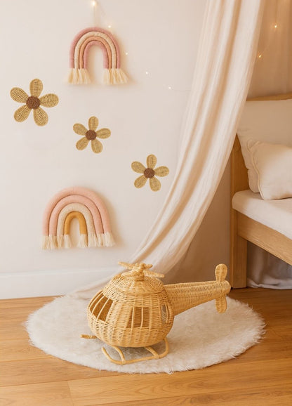Wicker helicopter toy on a white rug with decorative flowers and rainbows on the wall. The helicopter is a kids play toy and good for a birthday idea. 