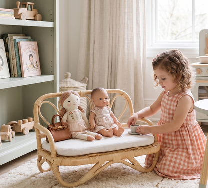 Child playing with dolls on a small wicker table in a bright room.