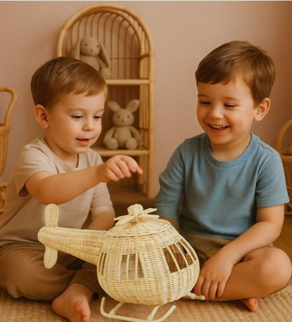 Two young boys playing with a woven toy helicopter in a warm, indoor setting. Plush toys sit on a shelf in the background. 