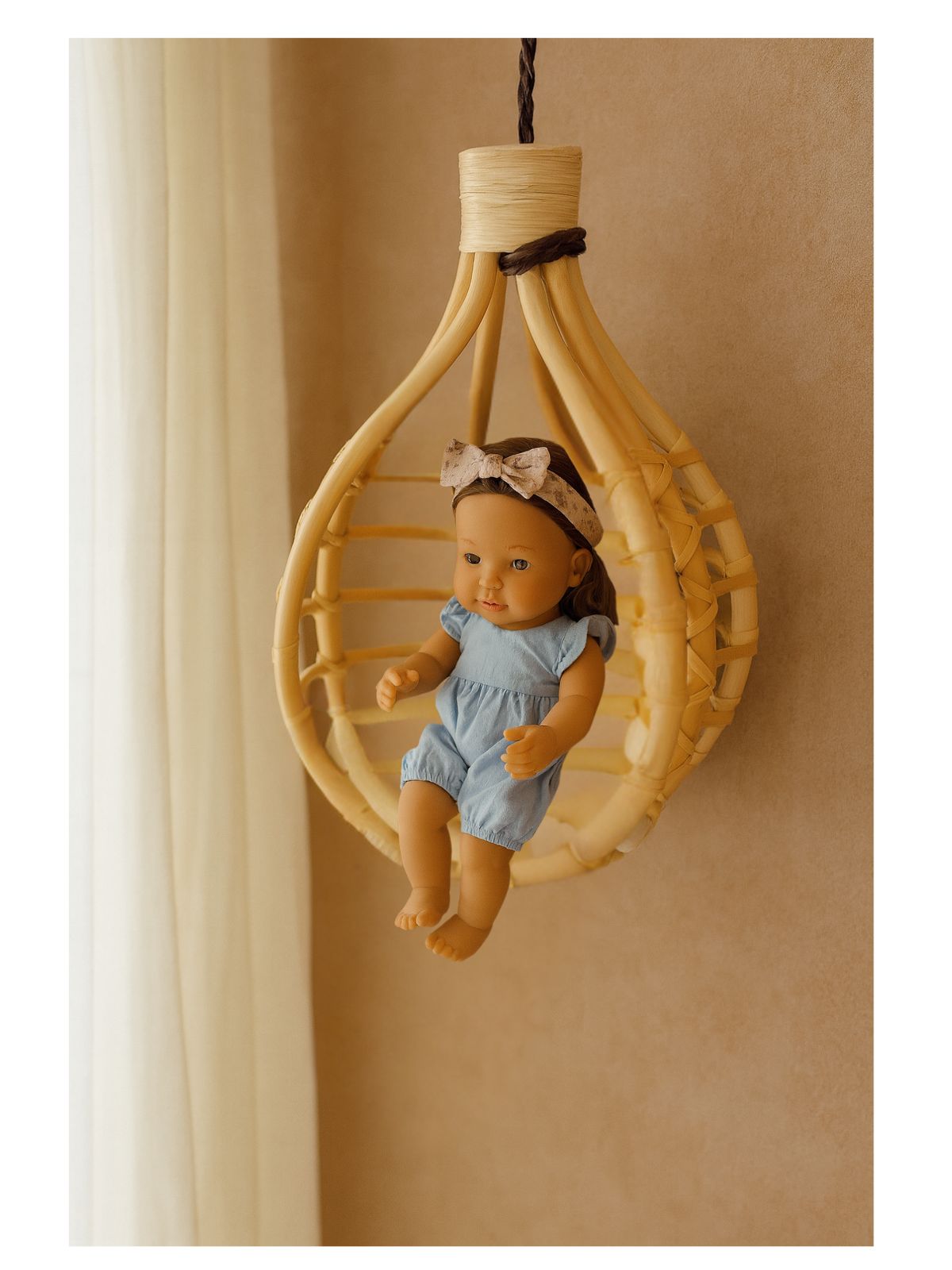 Rattan hanging chair wall decor for kids, used as a display for dolls and plush toys in a cozy playroom.