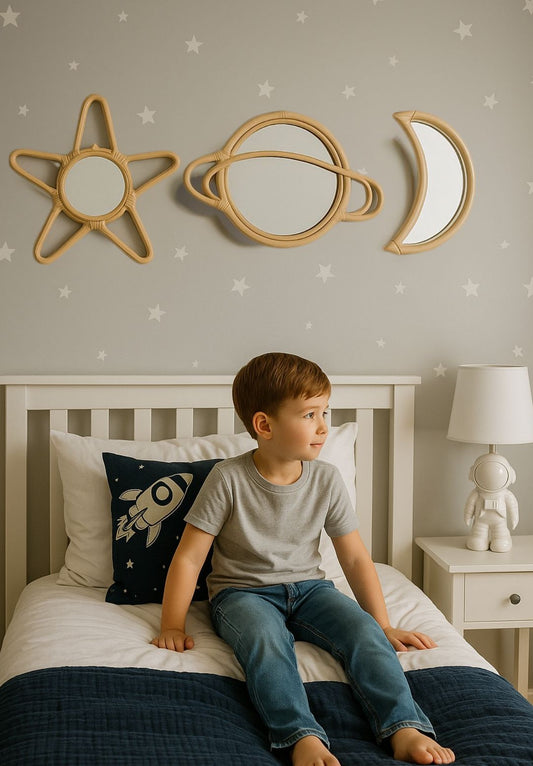 Child sitting on a bed with decorative mirrors shaped like stars, planets, and moons on the wall. An astronaut lamp sits on his side desk.