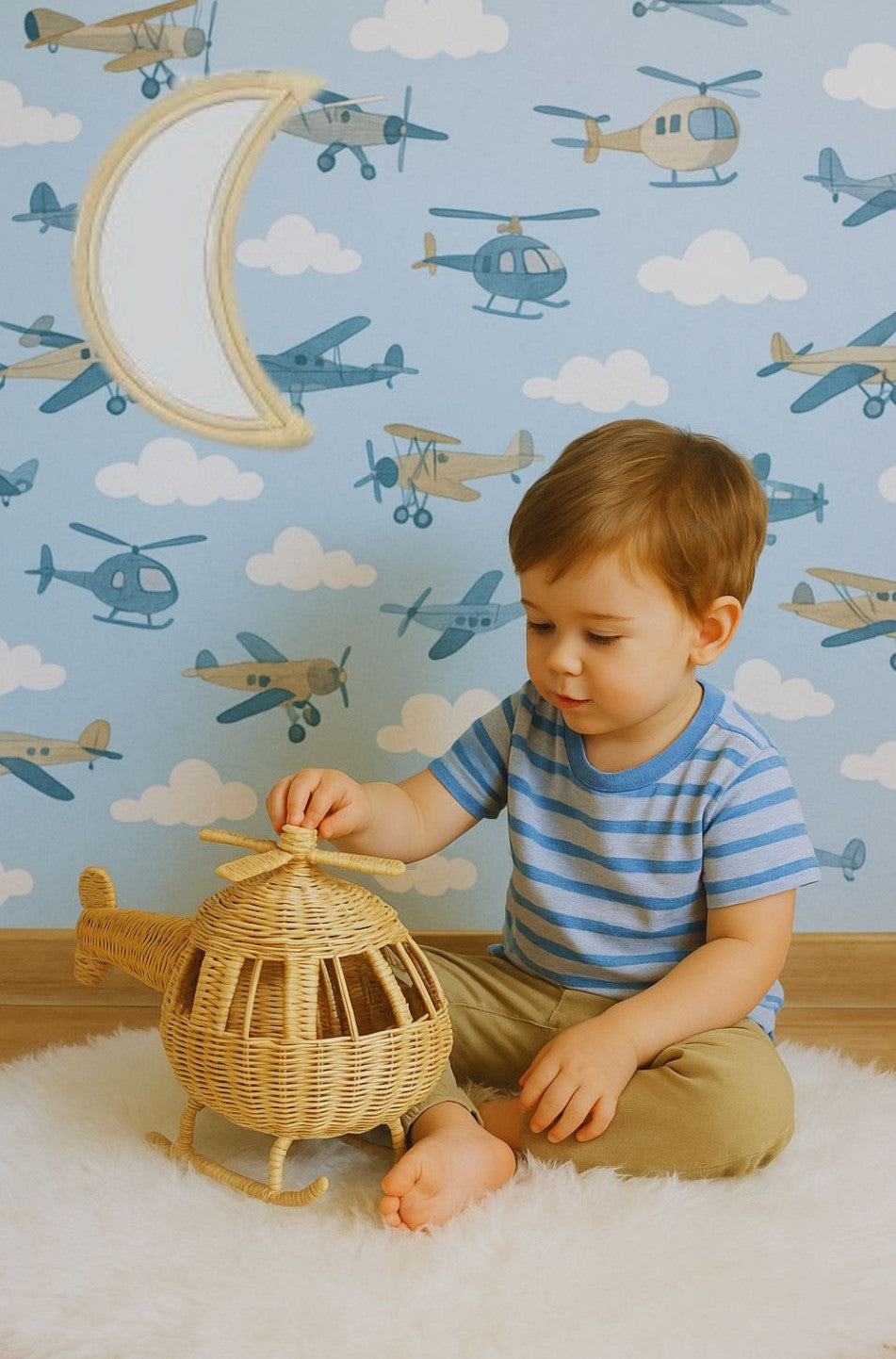 Child playing with a toy helicopter in front of a wall with airplane-themed wallpaper. Also on the wall sits a moon shaped mirror. 