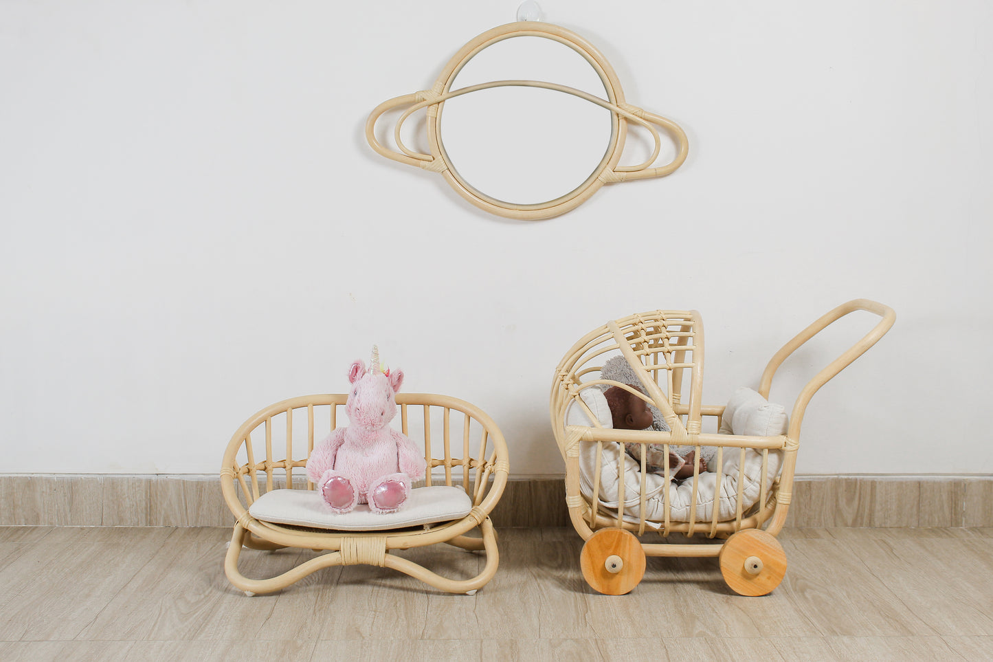 Wicker baby chair and pram with a pink plush toy on a light wooden floor.