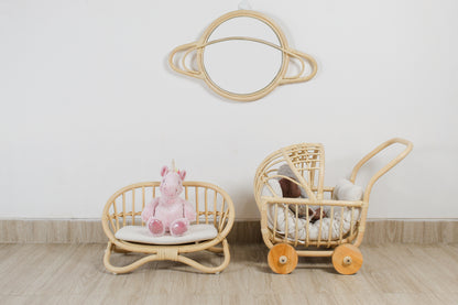 Wicker baby chair and pram with a pink plush toy on a light wooden floor.