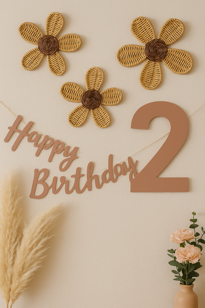 A set of 3 rattan wall decor flowers sitting on a pink pastel wall. It has a sign saying happy 2nd birthday. Beside this is a pot of flowers, roses, and dried flowers. It is a pretty scene. 