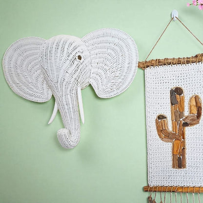 Woven elephant head and wooden cactus wall art on a light green background