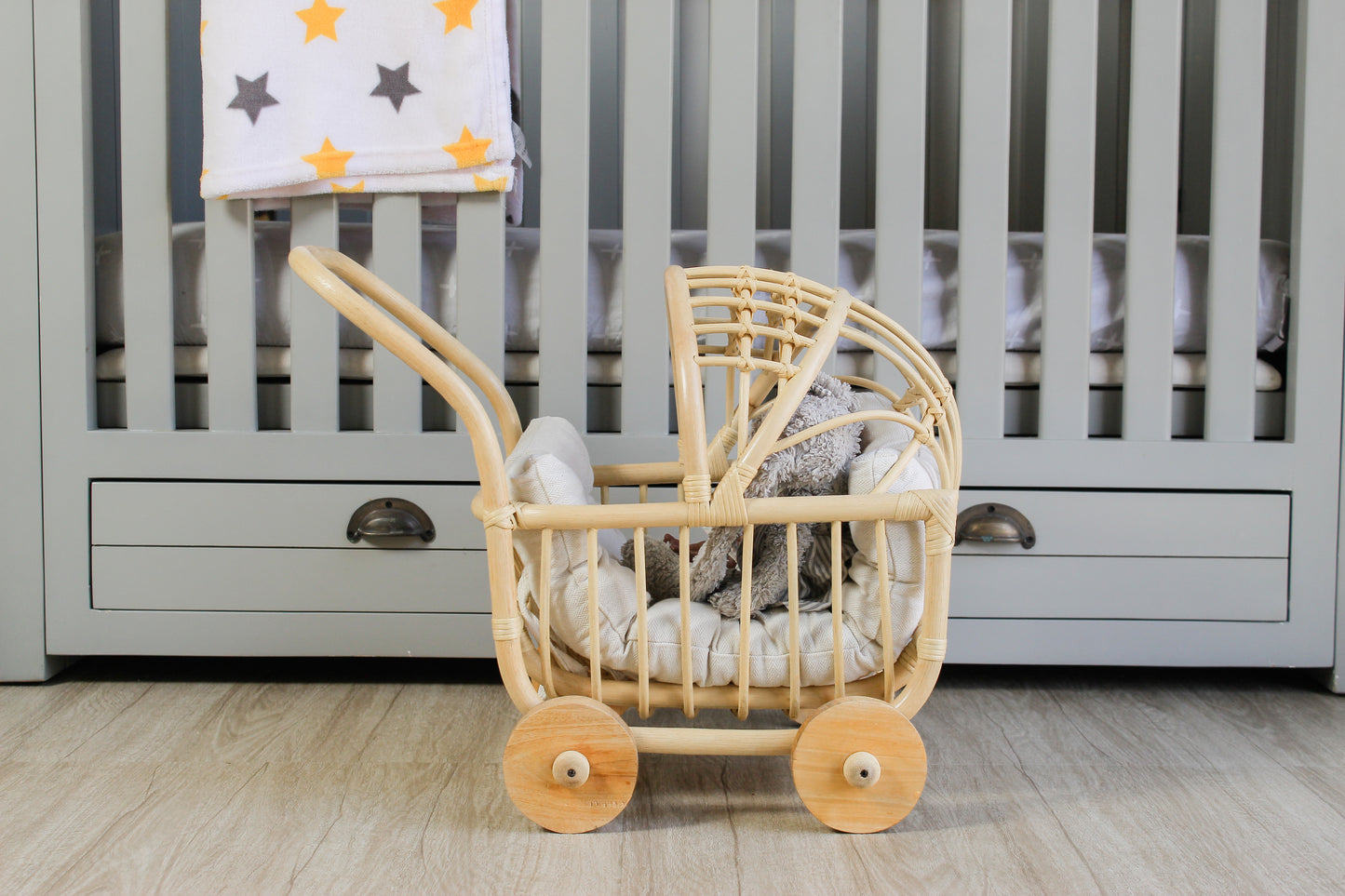 Wooden made doll stroller with spinning wheels in front of a baby crib