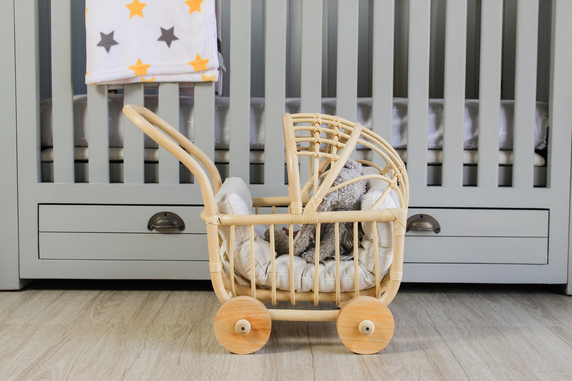 Wooden made doll stroller with spinning wheels in front of a baby crib